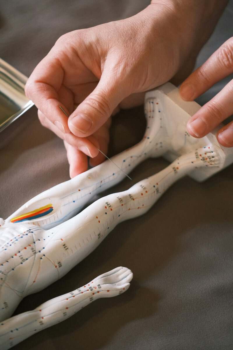 Close-up of hands threading a needle through a white fabric with printed measurement lines and colored dots.